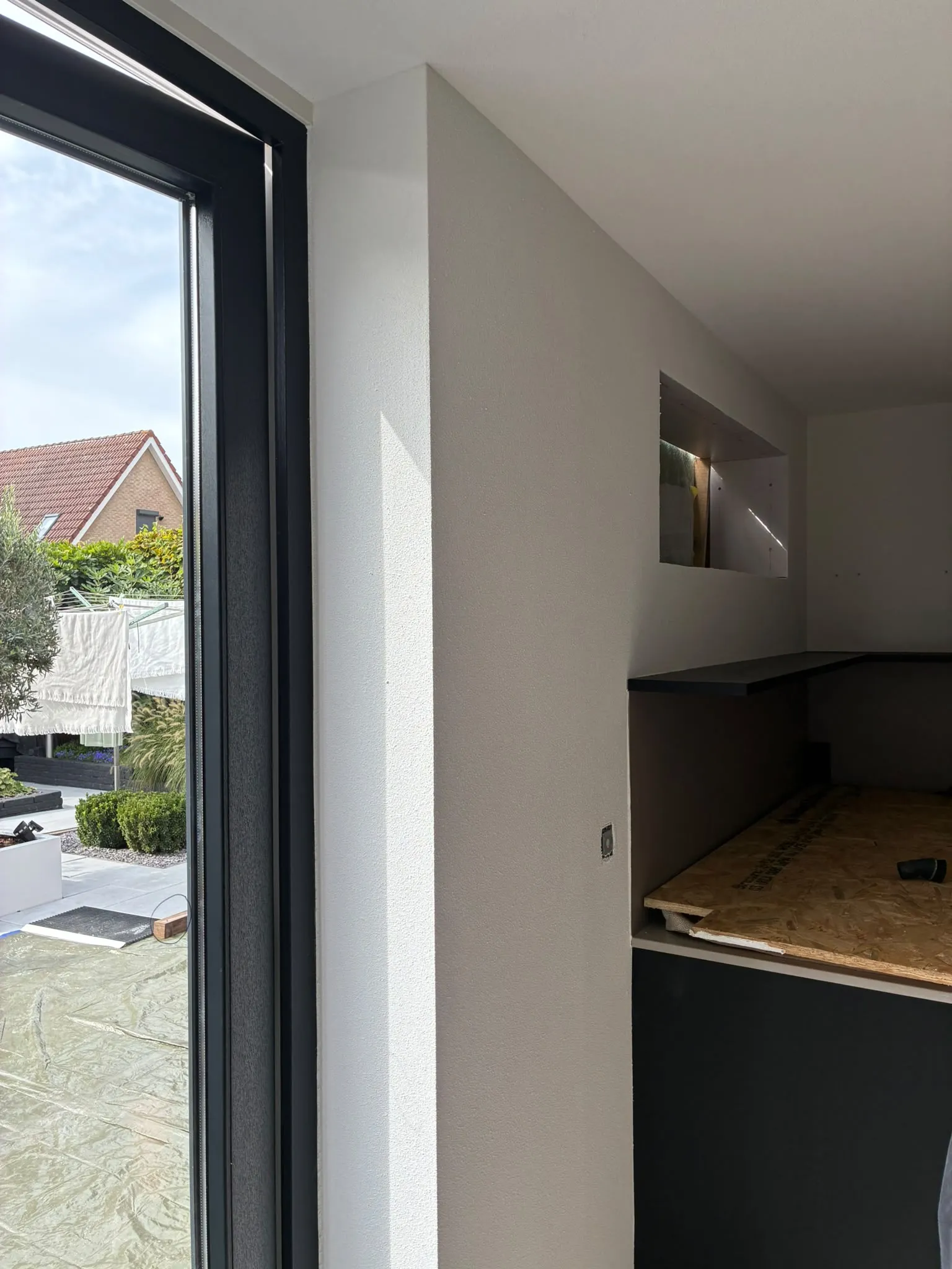 Gespoten wand met verlichte nis naast een keuken in aanbouw