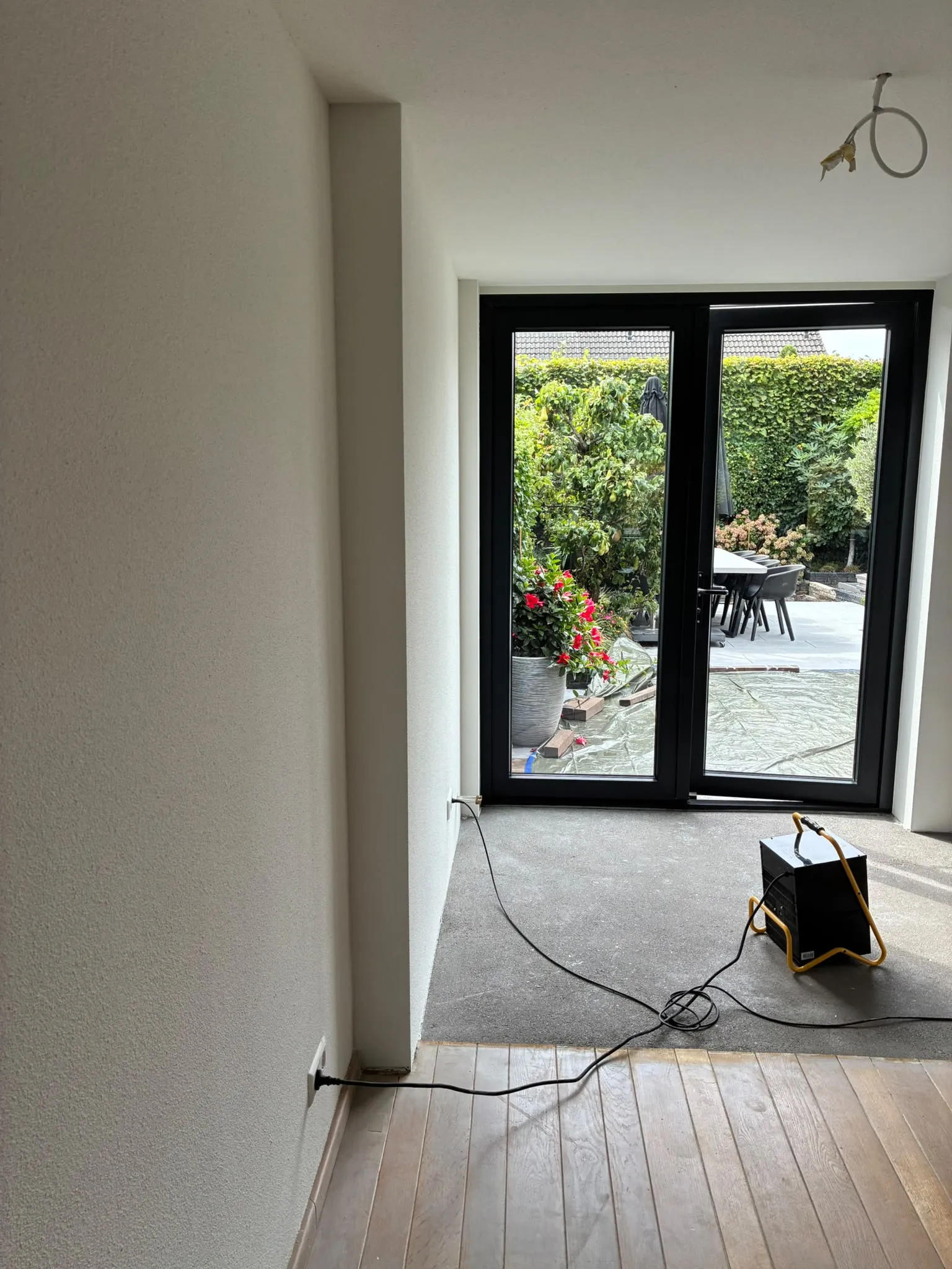 Lichte gespoten wand naast zwarte tuindeuren met uitzicht op de tuin